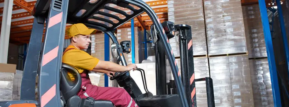 A forklift operator moving palletized goods inside a warehouse.